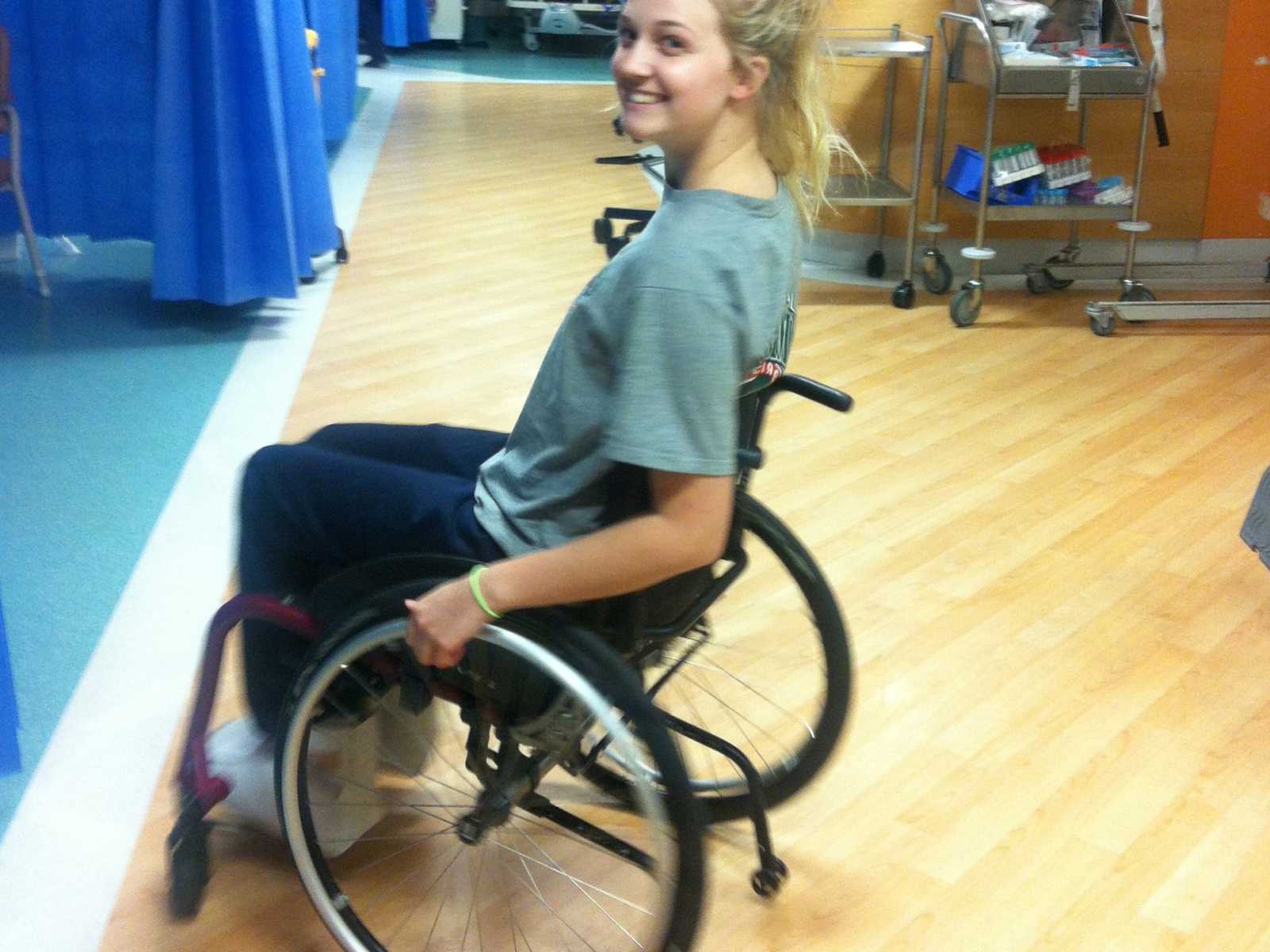 Paraplegic woman in wheelchair looks over shoulder smiling in hospital