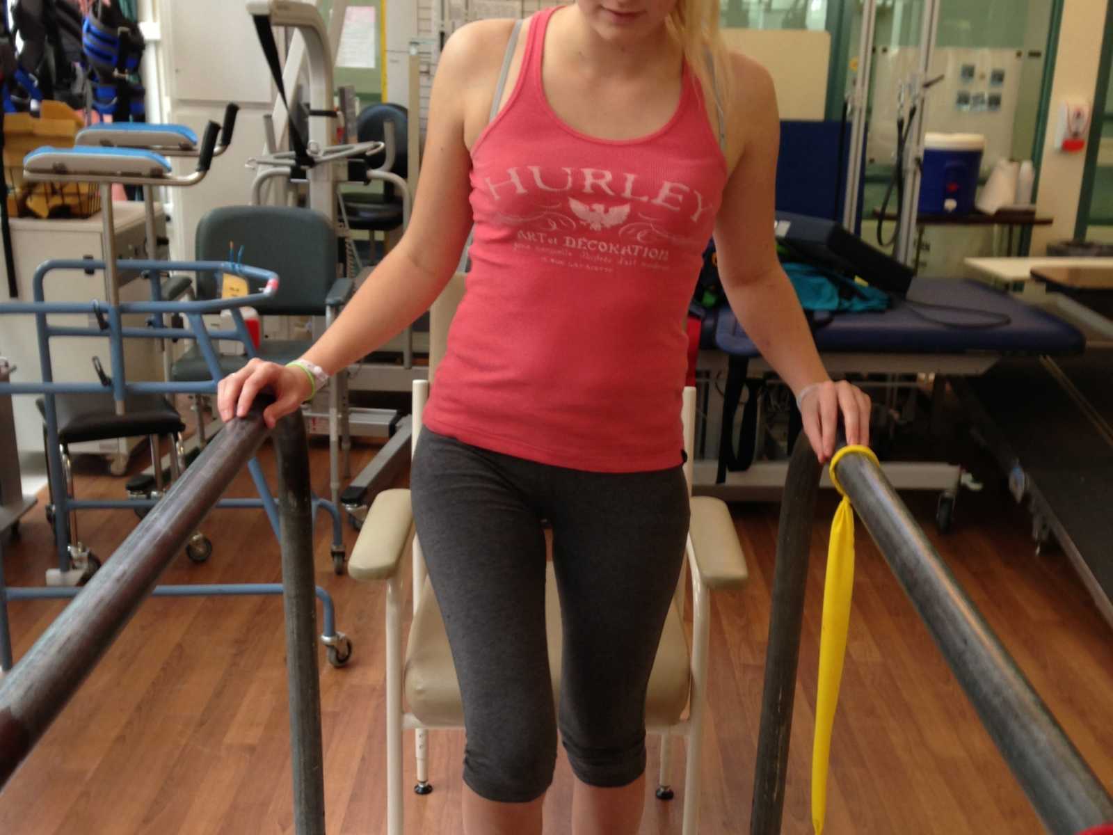 Paraplegic woman in physical therapy standing in-between to bars