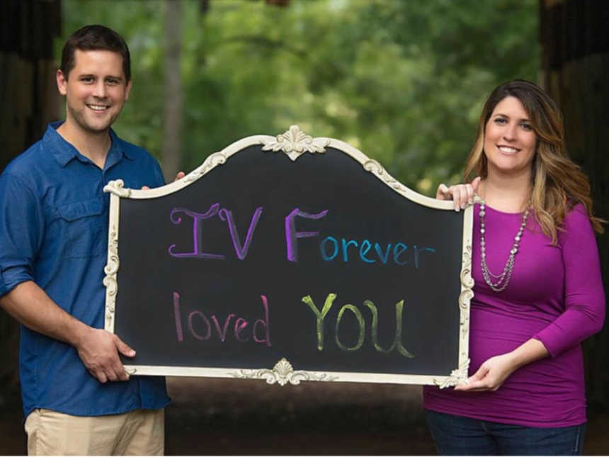 Husband and pregnant wife hold sign that says, "IV Forever Loved You"