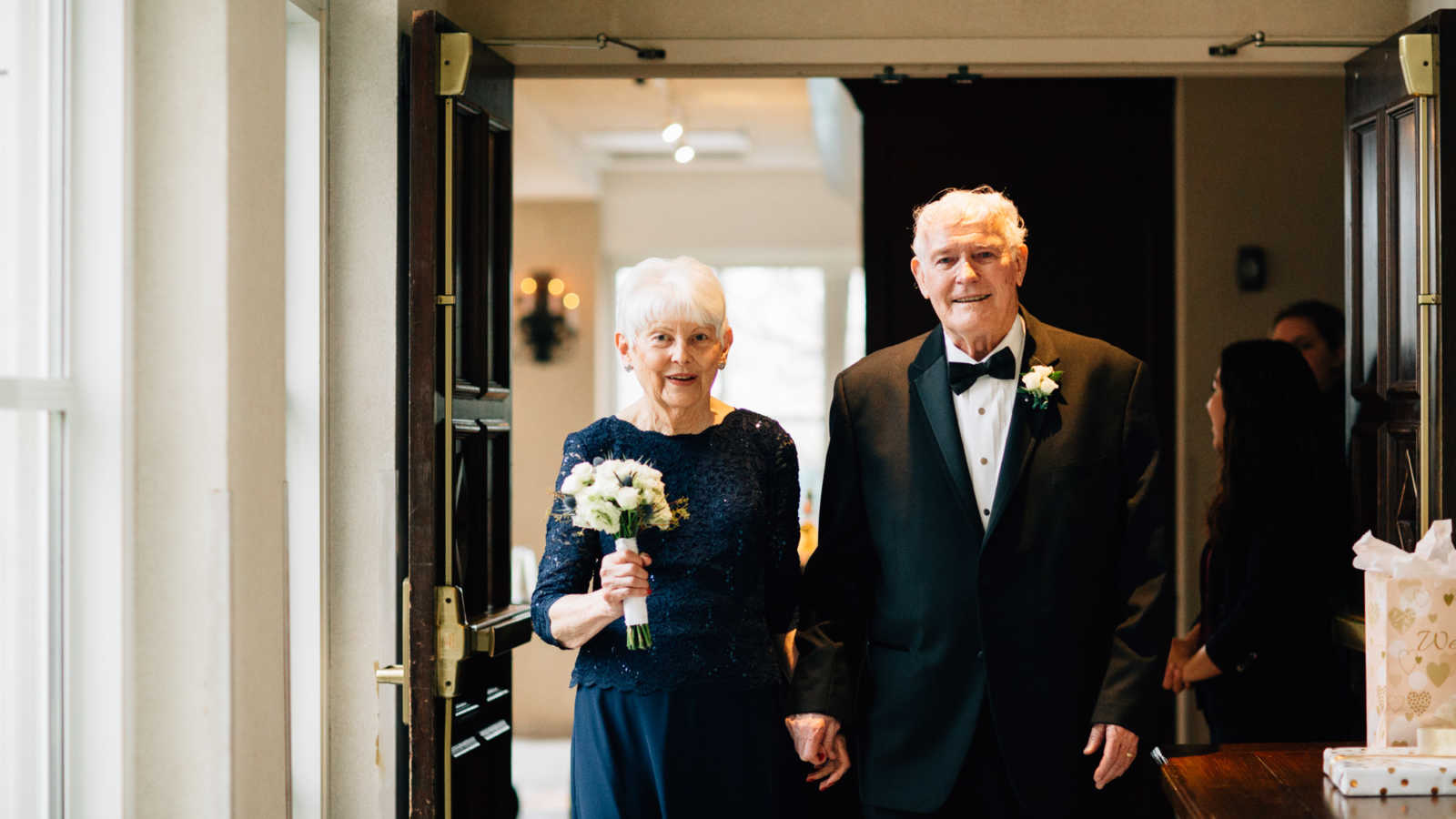 83 year old groom and 77 year old bride smile as they walk hand in hand