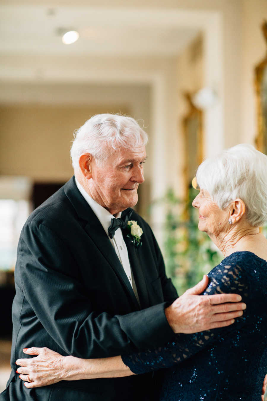 Elderly bride and groom hold each other in their arms staring into each others eyes
