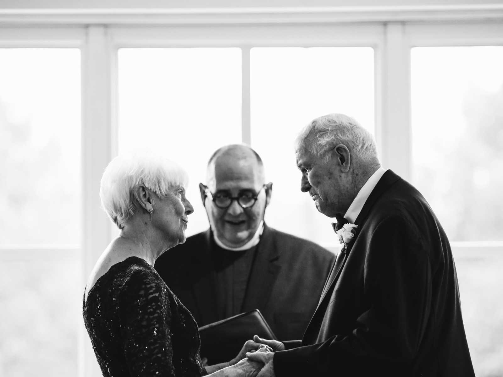 Elderly bride and groom stand hand and hand looking into each others eyes during wedding ceremony