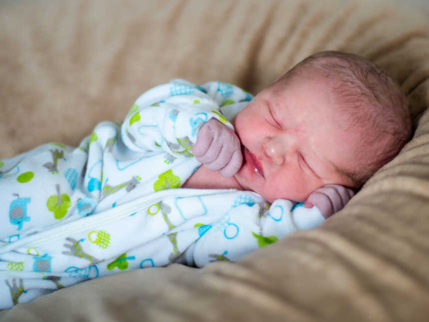 Newborn who was encapsulated in sac at birth sleeping in onesie with threes and elephants on it