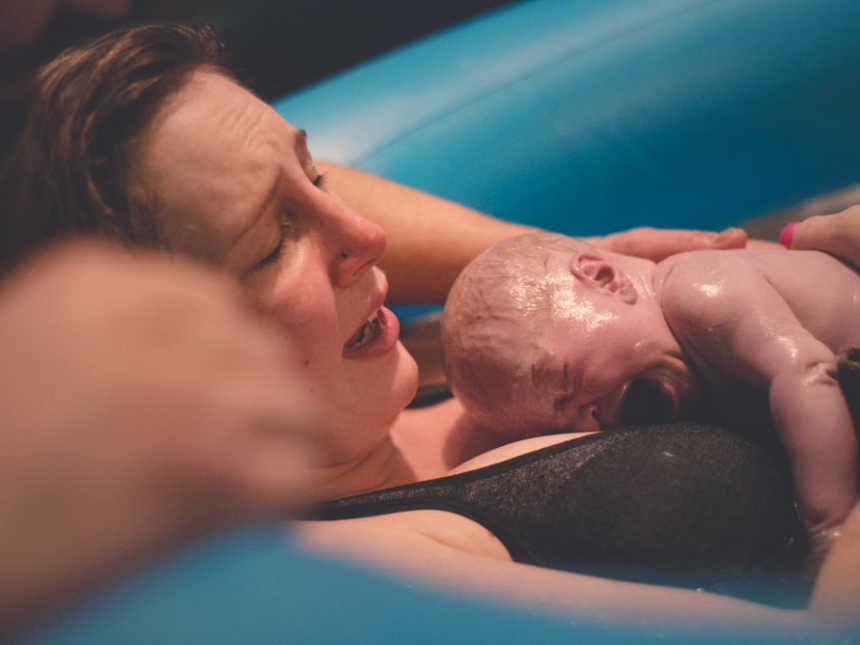 Woman who just gave birth to son encapsulated in his sac lays against birthing pool holds him to her chest