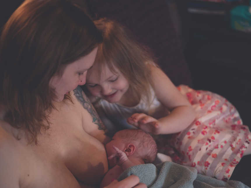 First born touching baby brother's head while he is breastfeeding