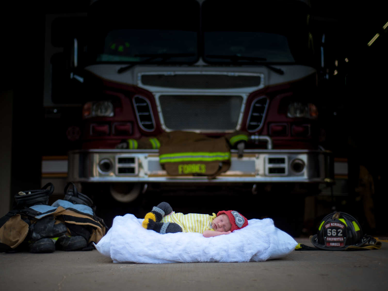 Newborn baby of fire fighter asleep on blanket in front of fire truck