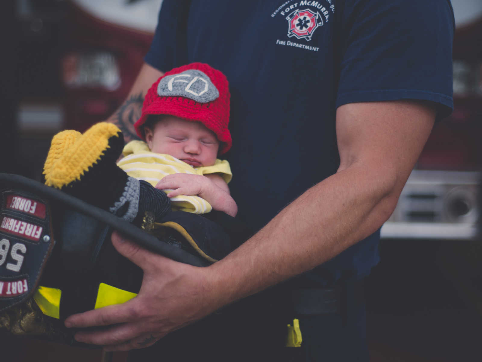 Fire fighter father holds newborn son in fire fighter hat after returning home form fighting fires