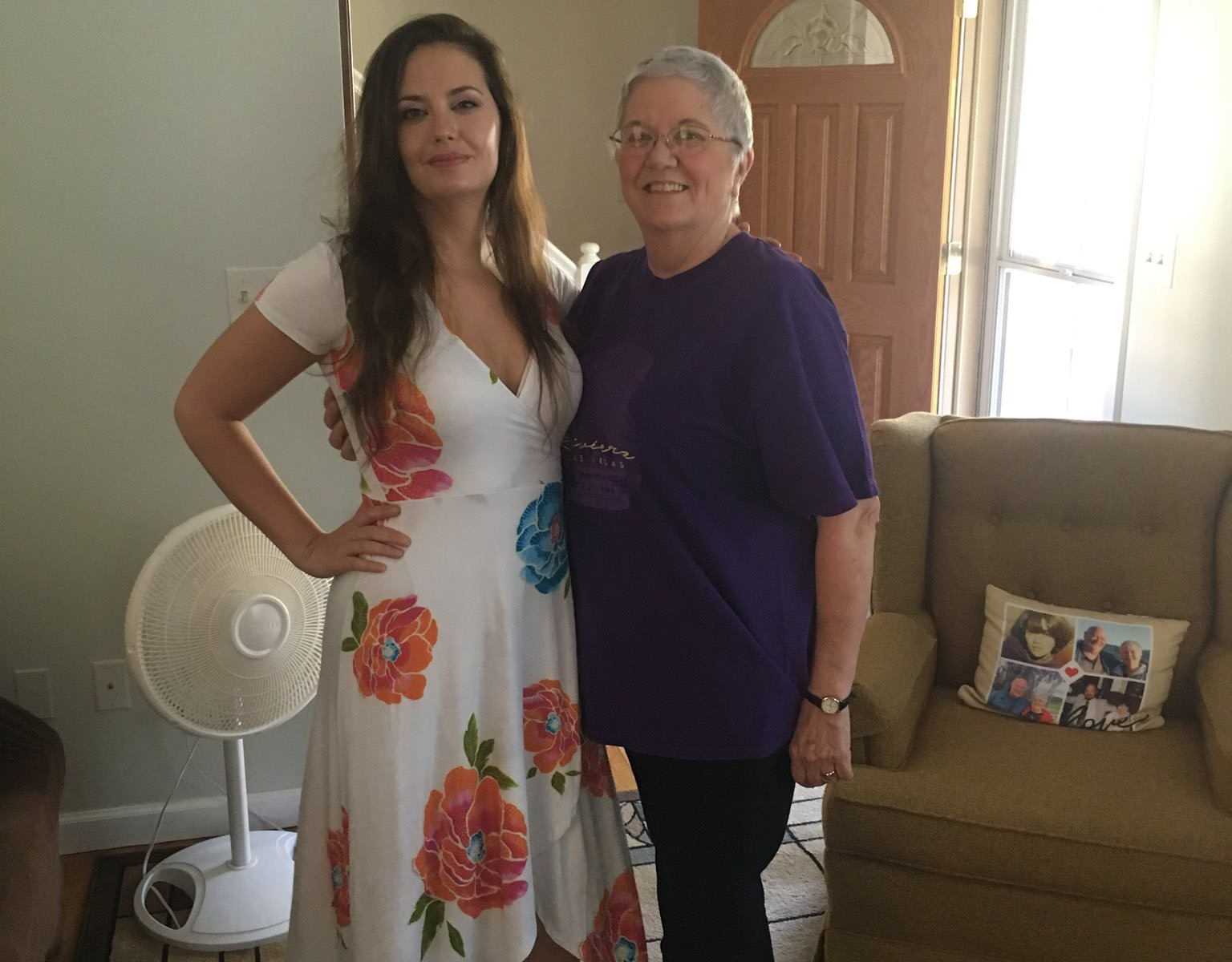 Woman with hand on her hip in floral dress smiles with arm around grandma who has small cell cancer