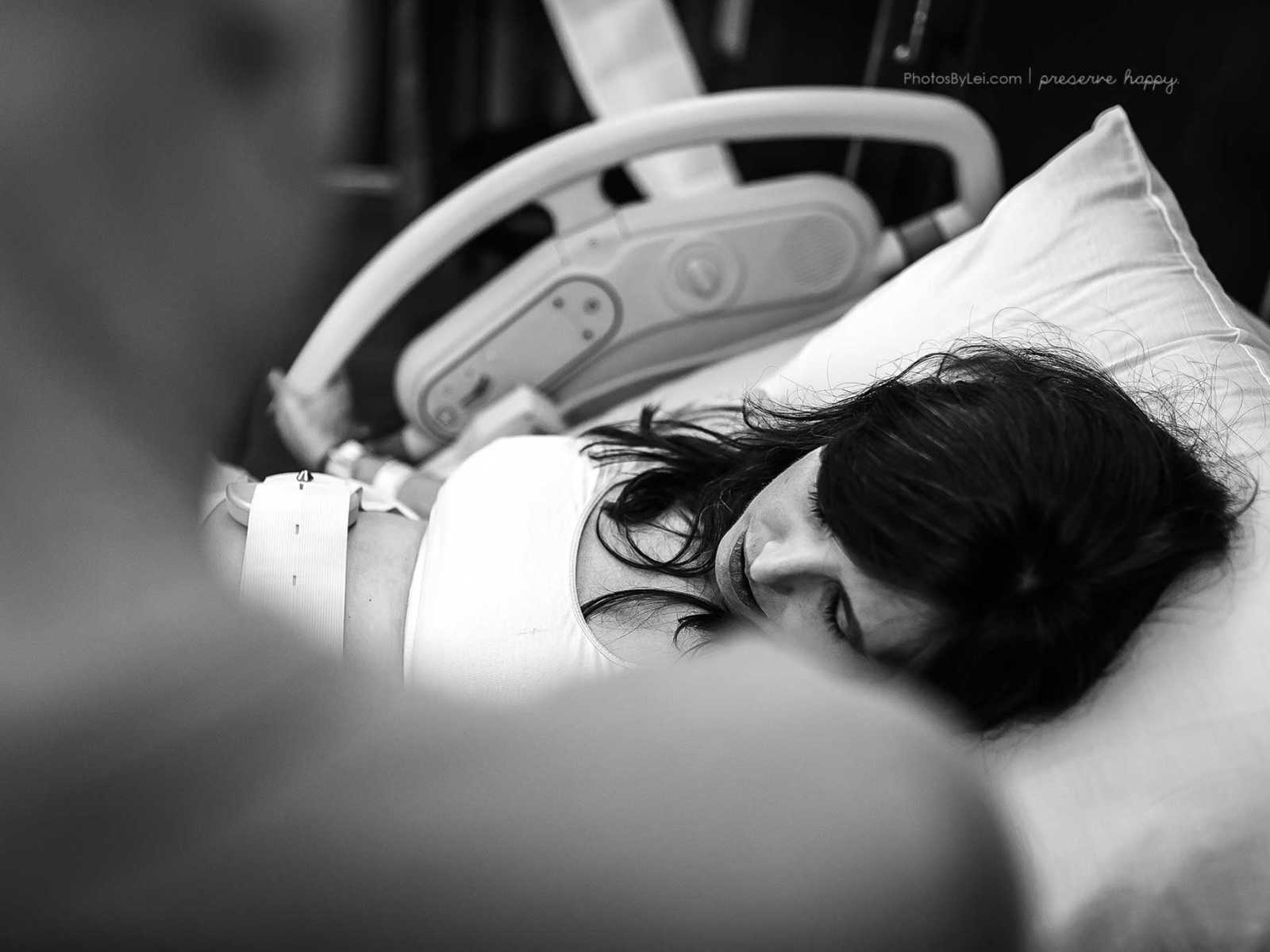 Pregnant woman with fetal monitor over stomach rests head on pillow in hospital bed