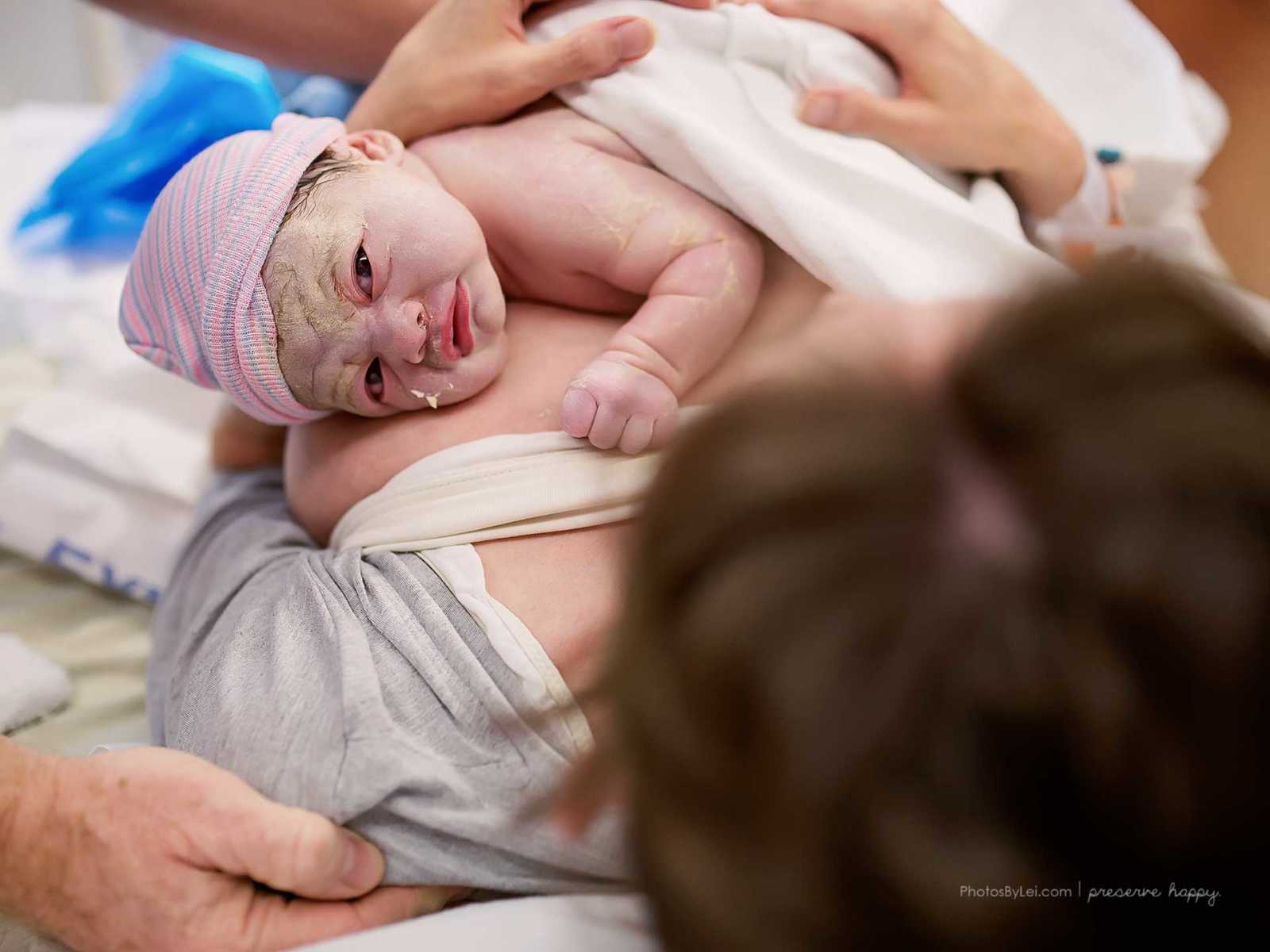 View from mothers head of newborn who was covered in amniotic fluid lying on mother's breast