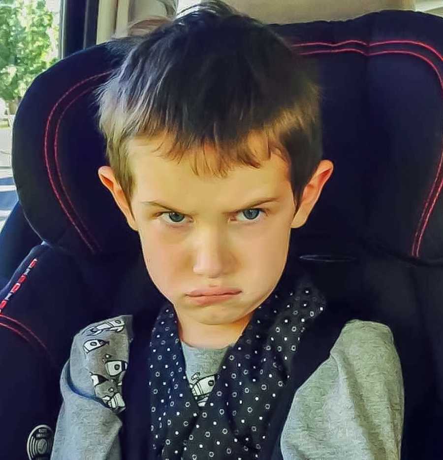Autistic boy sits in carseat with upset look on his face