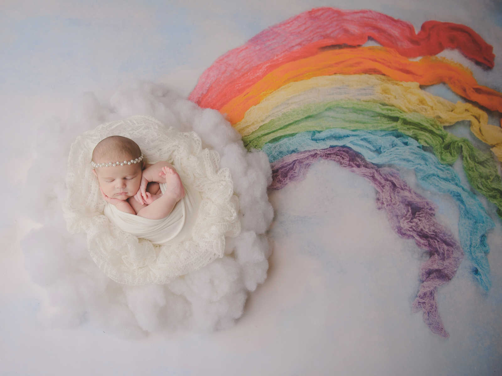 IVF baby asleep in white blanket at end of rainbow
