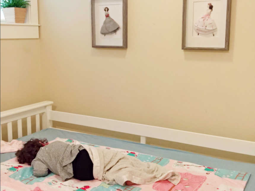 Little girl asleep under frames of paper dolls wearing her clothes from when she was a baby