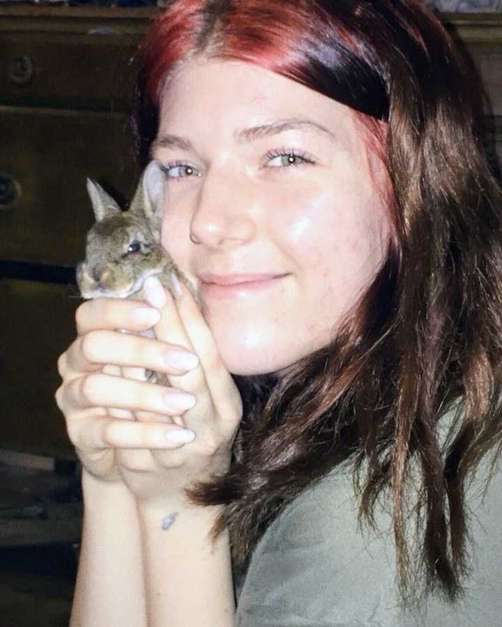 Woman smiles while holding baby bunny in both hands up to her cheek