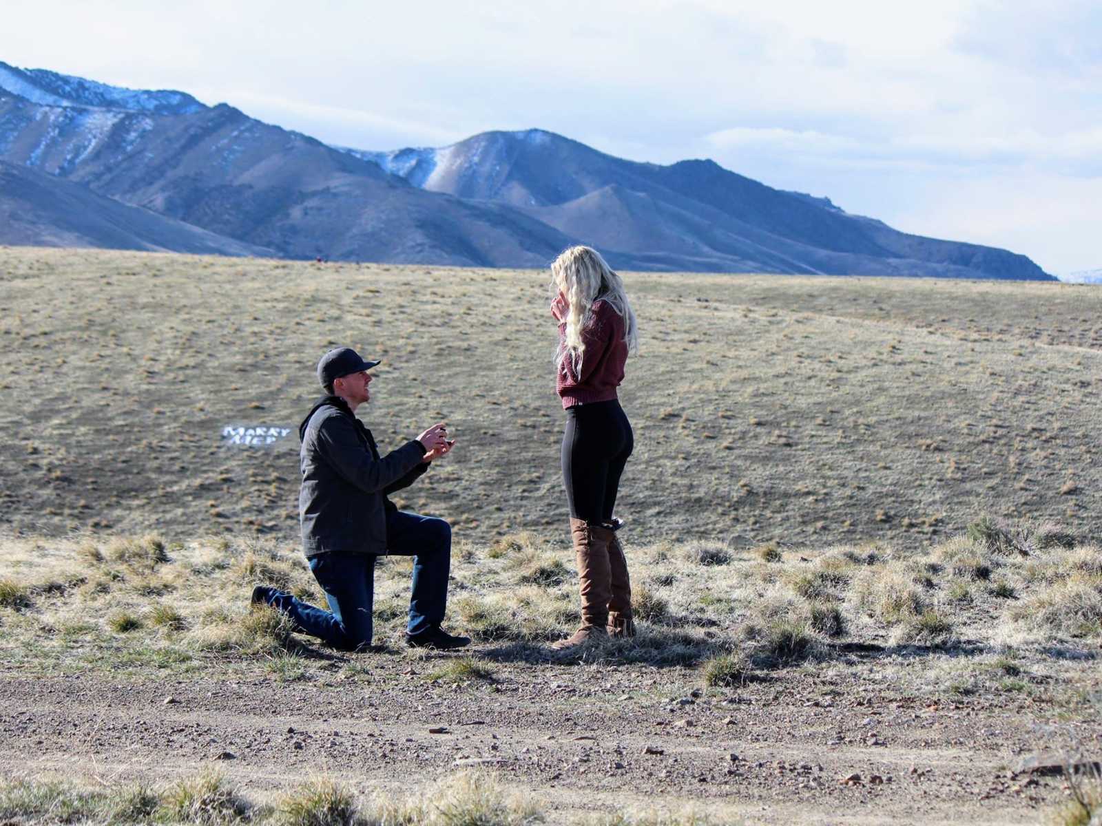 Man proposes to woman on plain with mountains in background