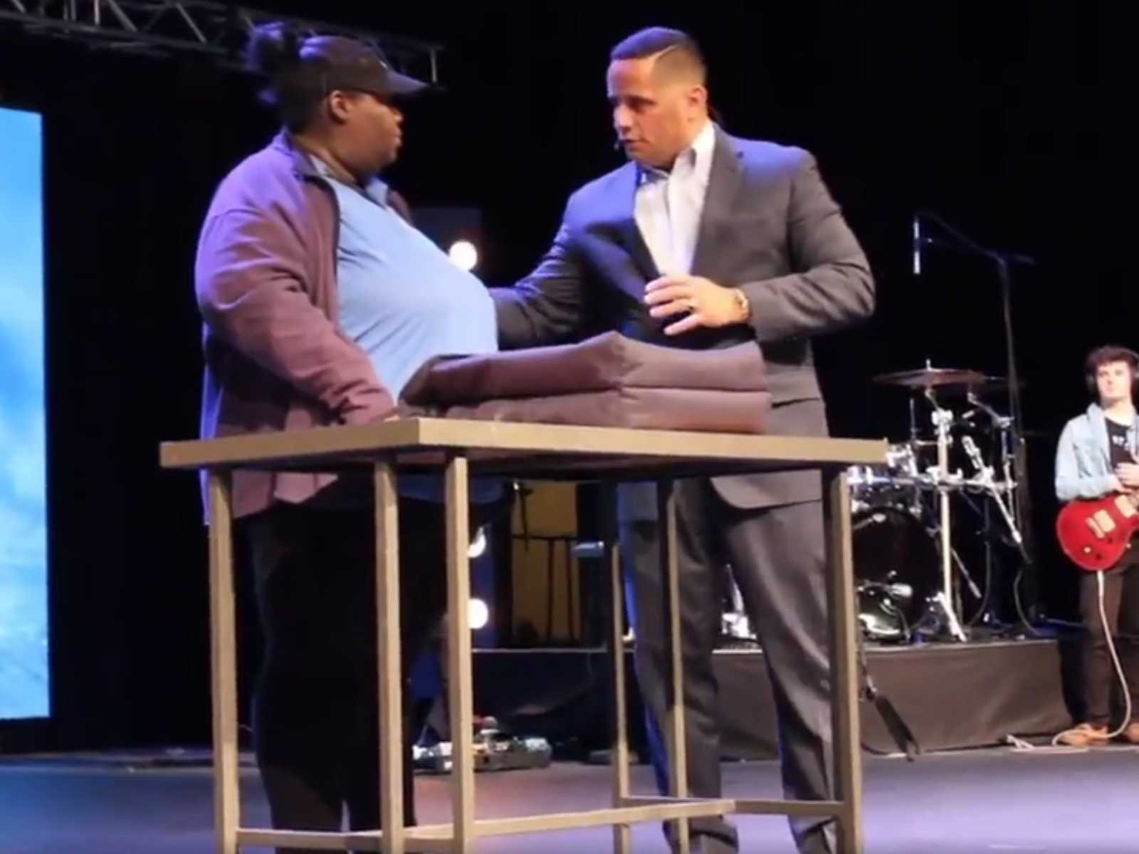 Single parent who works as a pizza deliverer standing on stage at church with pastor