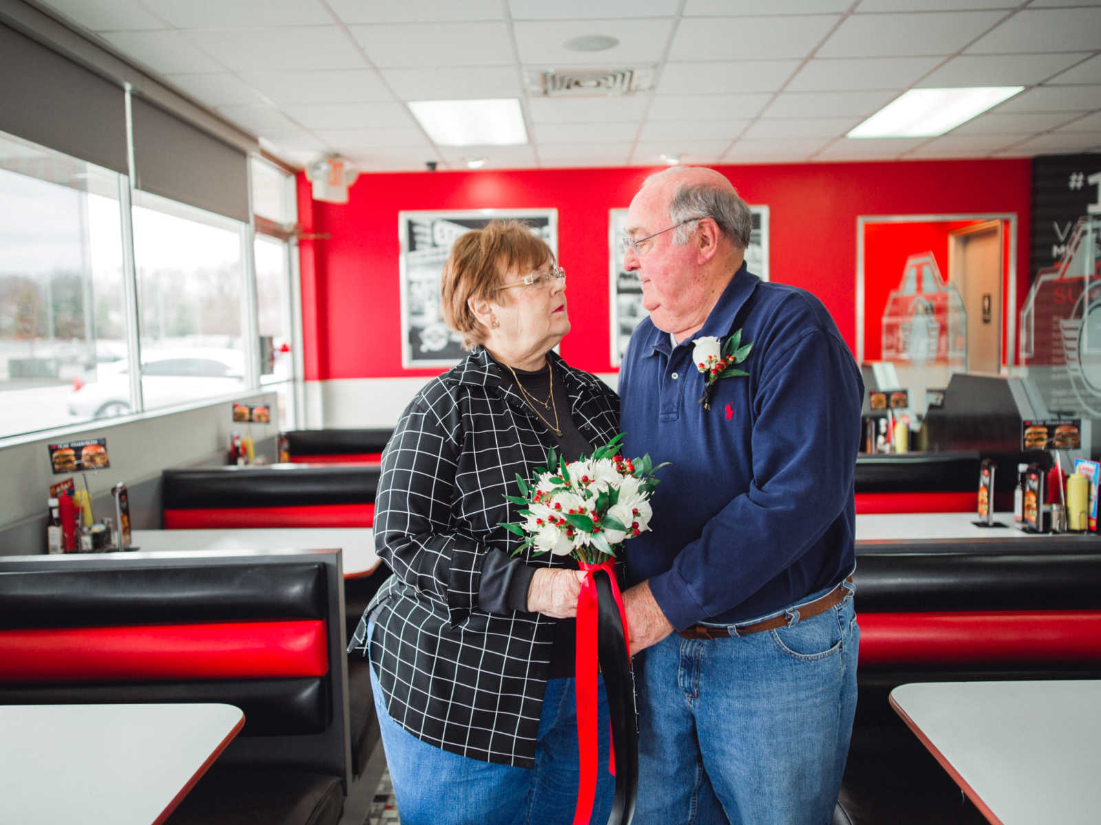 Husband and wife who met at Steak 'n Shake in 1962 stand holding a bouquet of flowers in restaurant