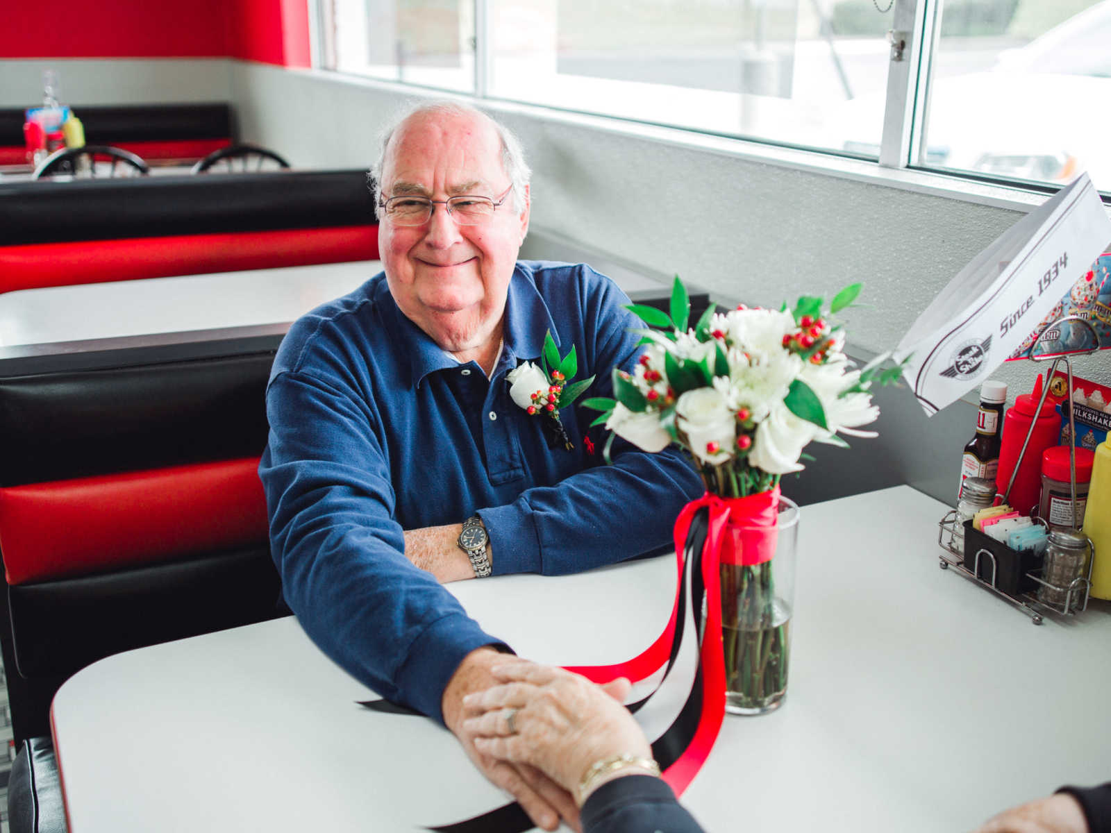 Husband smiles while holding hands with wife in Steak 'n Shake booth