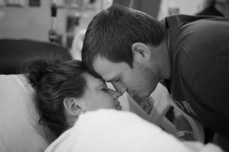 Husband and pregnant wife touch noses as he leans over her in hospital bed