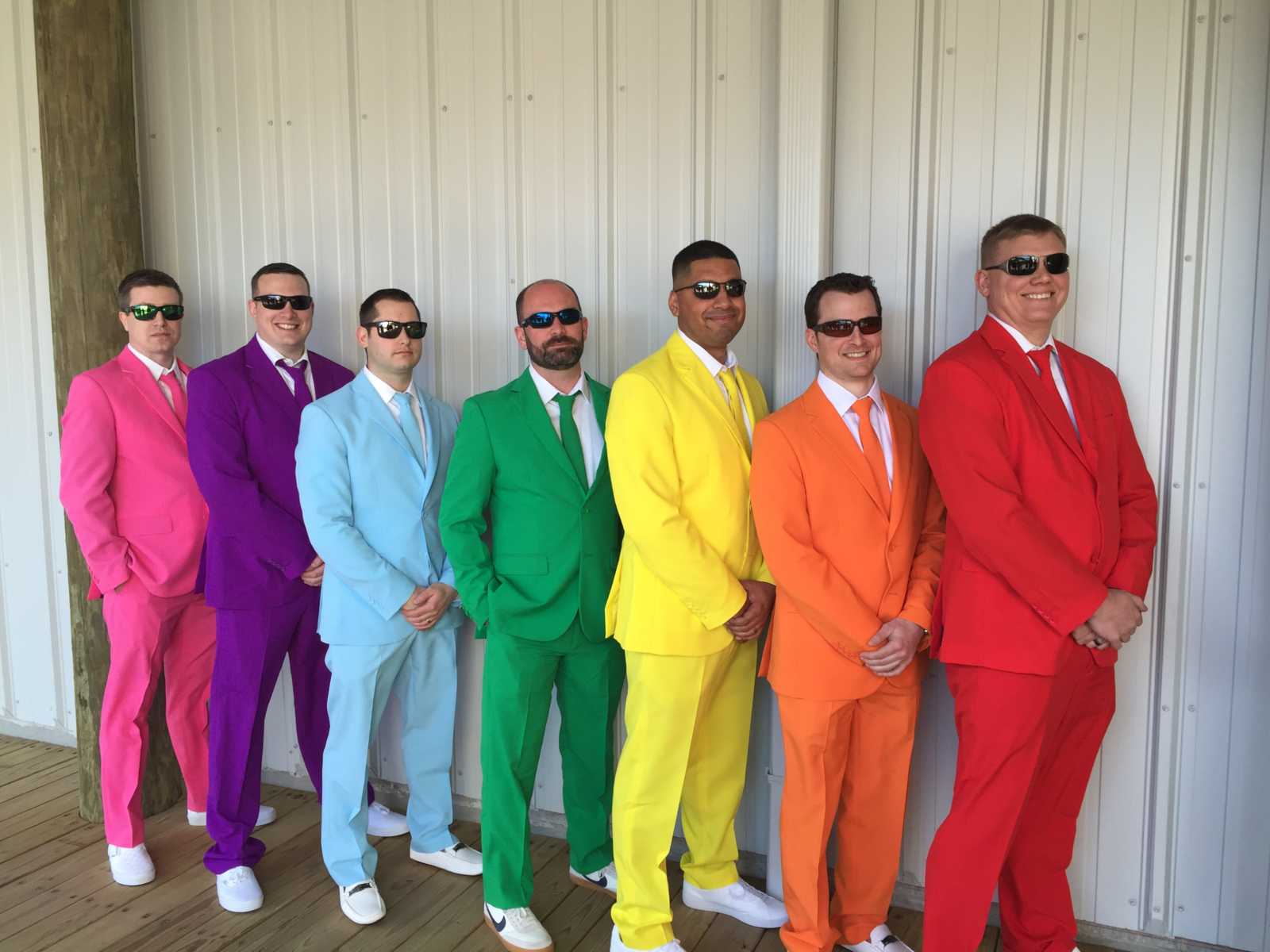 Men standing in line colorful suits in order of rainbow with sunglasses on