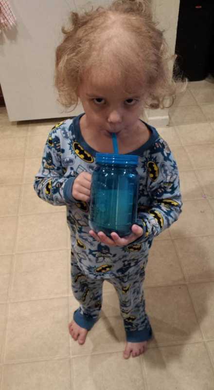 Boy with leukemia standing in kitchen in batman pj's sipping out of a straw
