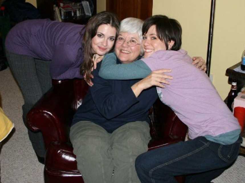 Woman with cancer sitting in leather chair with two granddaughters leaning over hugging her