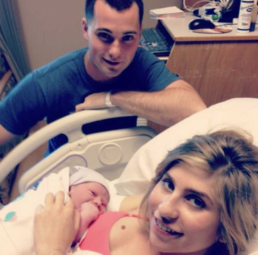 Woman lying in hospital bed with newborn to her chest with husband crouching down next to them