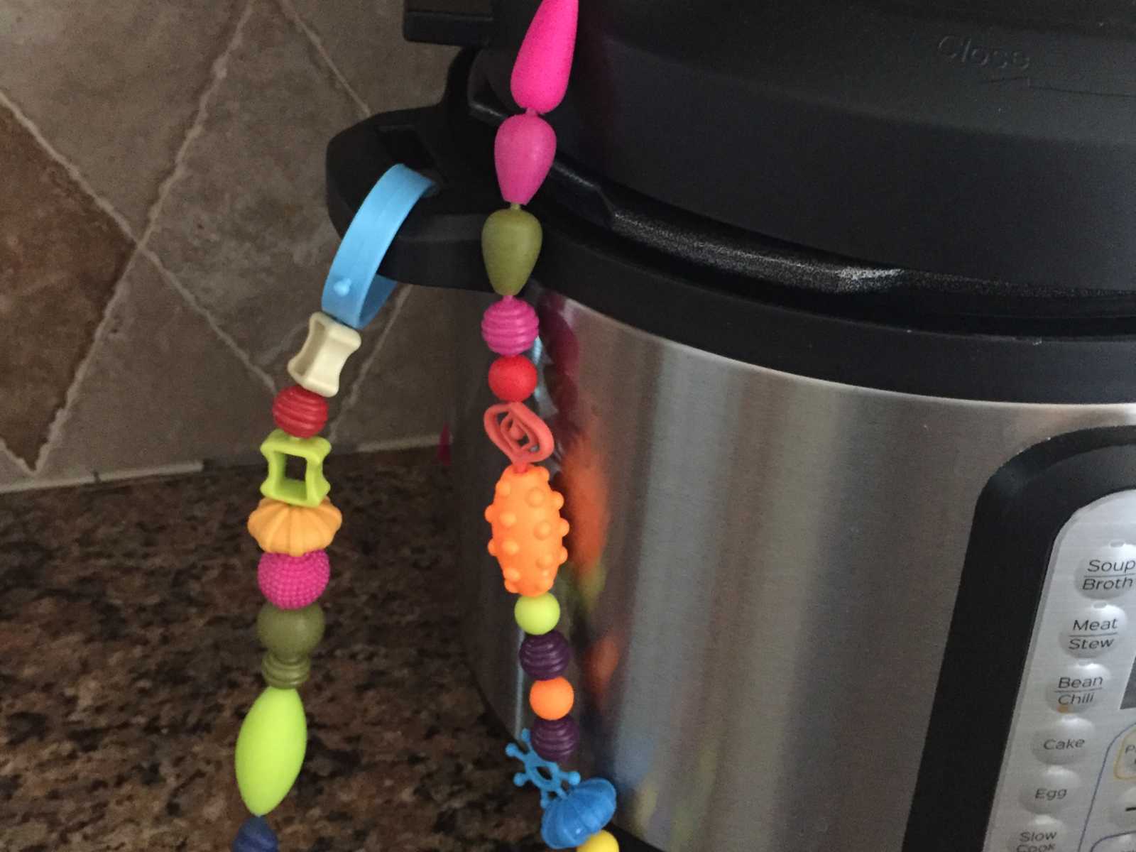 Instant pot sitting on kitchen counter with baby toys dangling off the lid