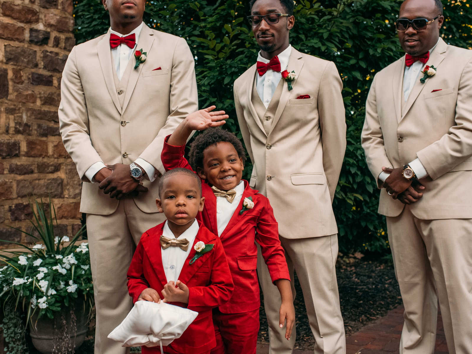 Little boy smiling and waving as he stands next to younger brother and groomsmen at mothers wedding