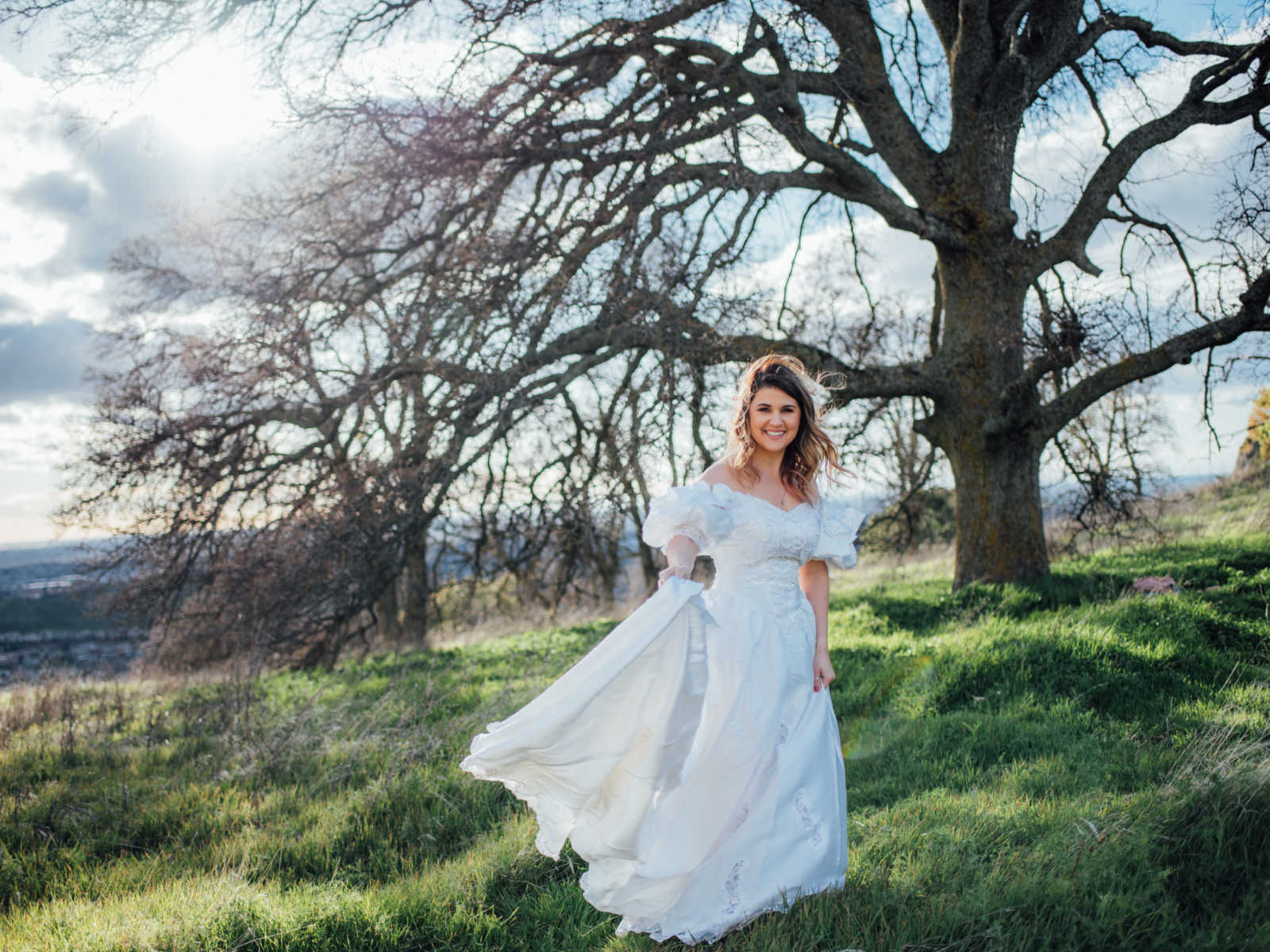 Daughter smiles wearing deceased mothers wedding dress in front of large tree