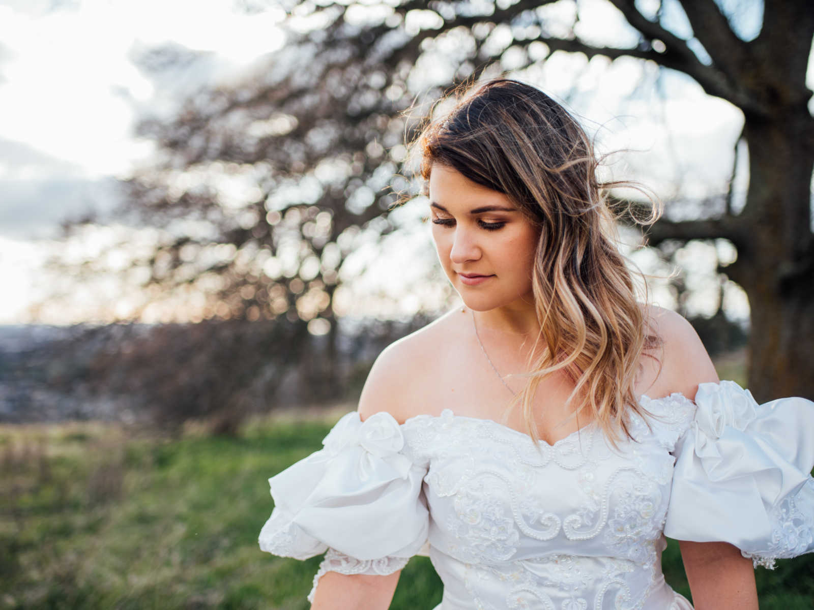 Close up of daughter wearing deceased mother's wedding gown looking down to the side