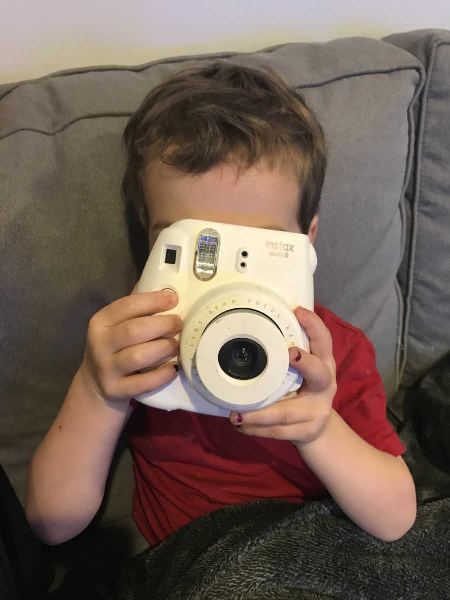 Little boy holding white polaroid camera up to his face