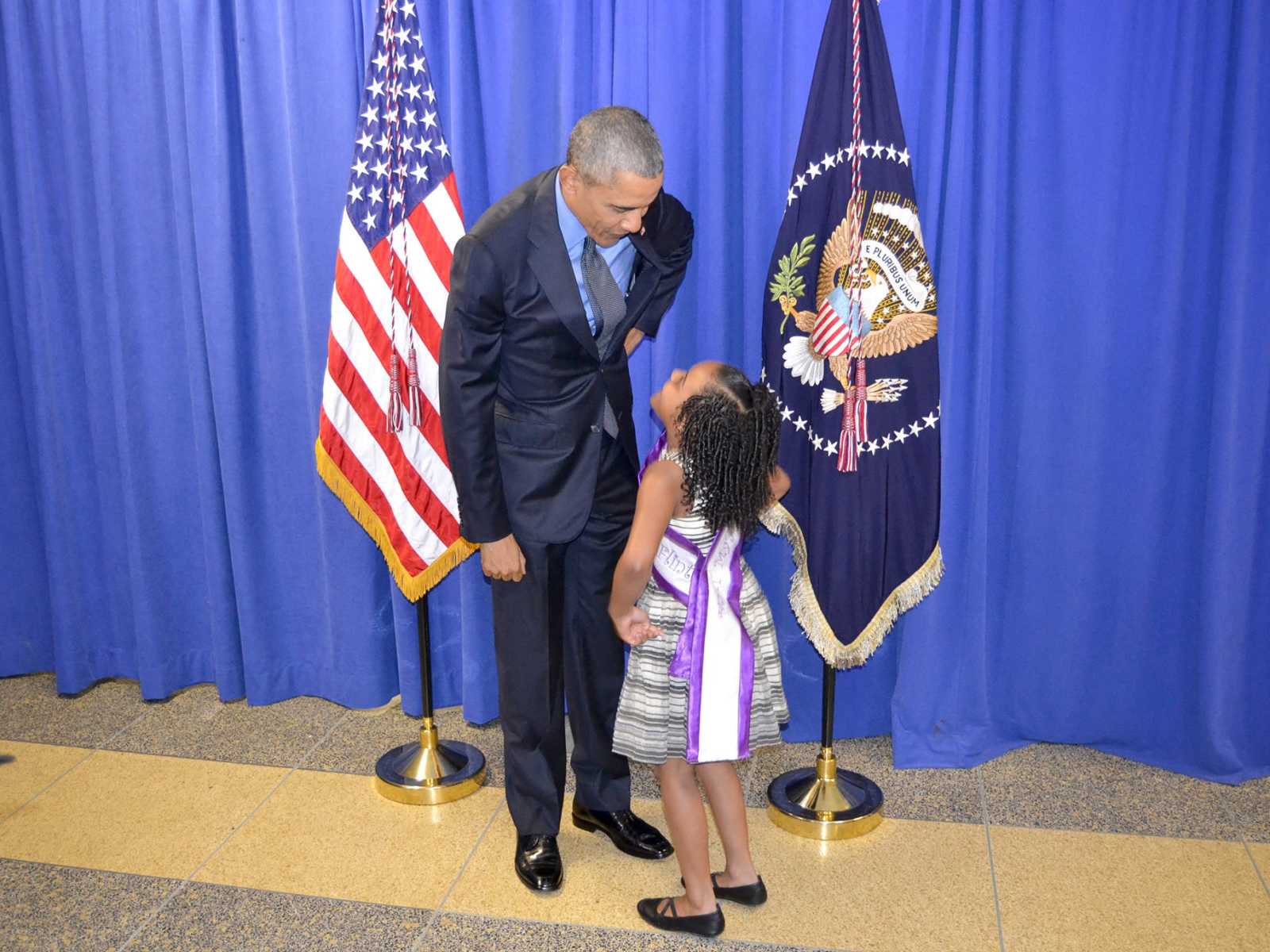 Little girl from Flint, Michigan standing looking up at Barack Obama with hand on her hips while he looks down at her