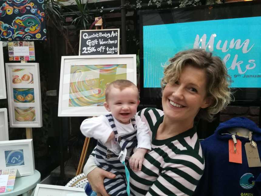 Woman who was a lawyer holds baby in arms in front of ultrasound paintings