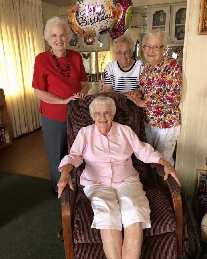 97 year old woman sits in chair with birthday balloon attached surrounded by three sisters