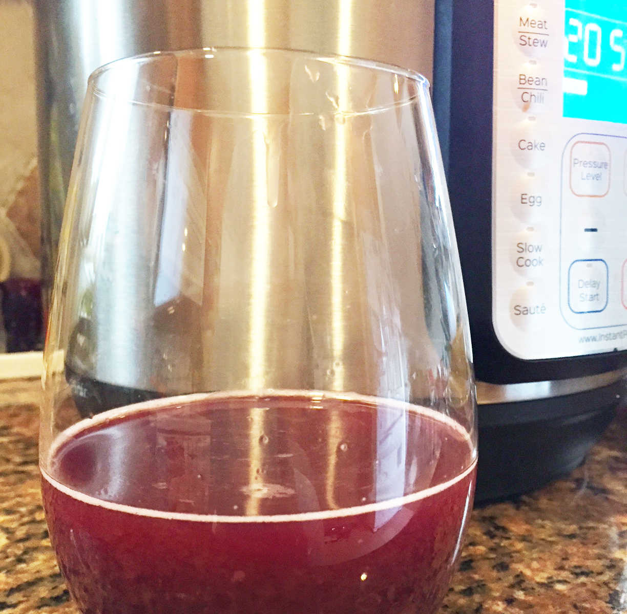 Stemless wine glass filled with red wine sitting on counter in front of instant pot