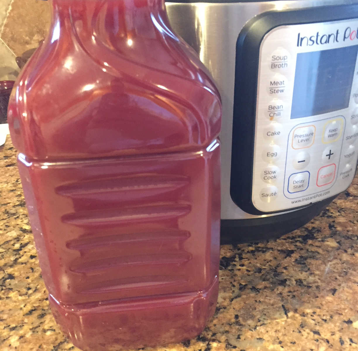 Clear juice jug filled with red wine sitting on kitchen counter next to instant pot