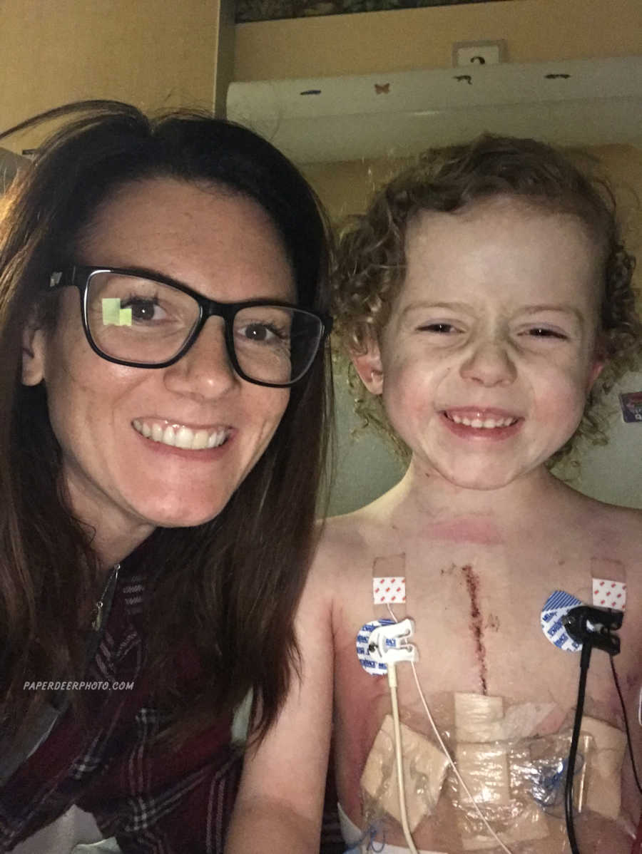 Mother smiles with son who just had third heart surgery with large scar on his chest in selfie