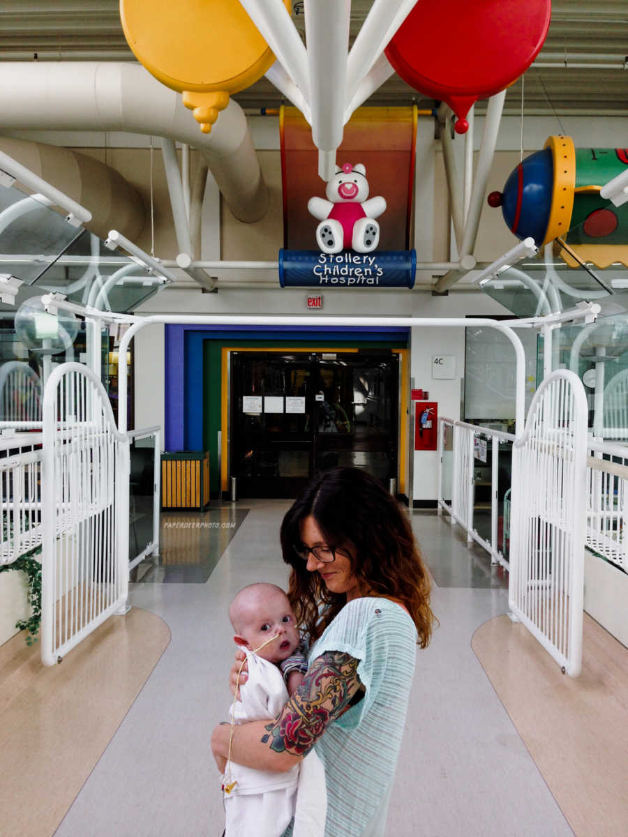 Mother smiling down at her son she holds after his second heart surgery in children's hospital