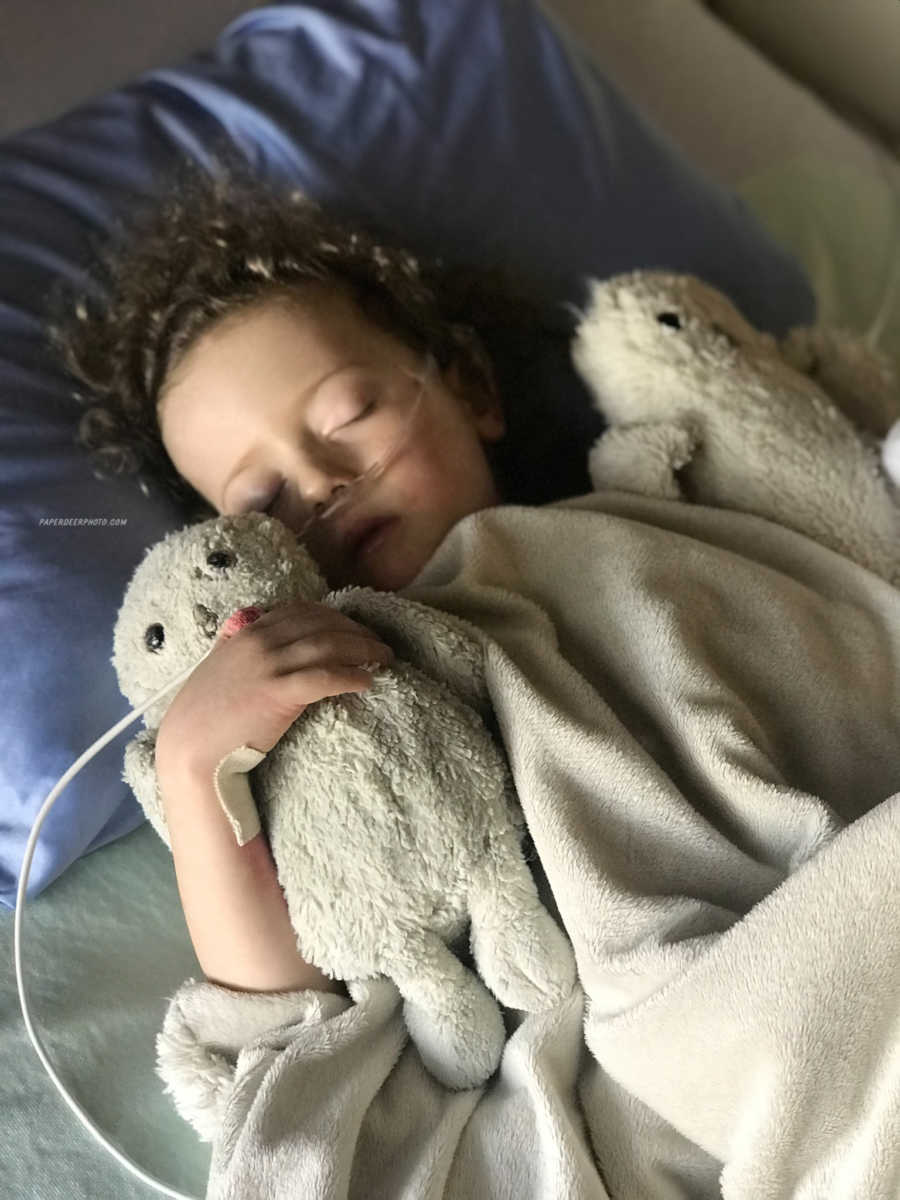 Four year old boy sleeps in hospital bed with a stuffed animal on either side of him after third heart surgery