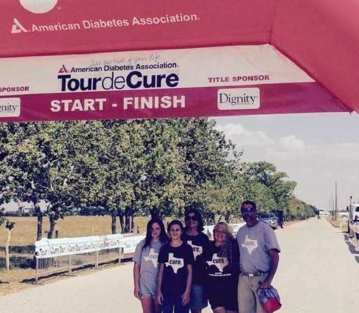 Pregnant woman with diabetes stands with family under pink arch that says, "tour de cure"