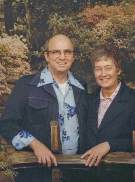 Wife wearing diamond ring that was found on farm smiling next to husband leaning on wooden plank