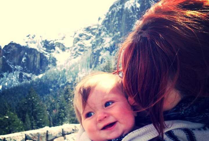 Mother kissing smiling baby with mountains in background