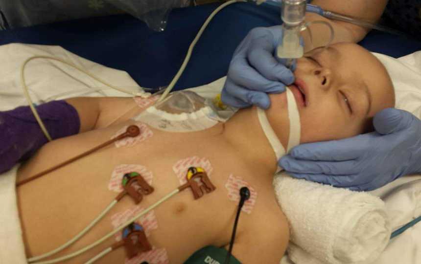 Boy with leukemia lying down while someone adjusts hose in his mouth