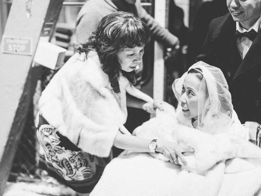 Terminally ill bride wrapped in blanket being pushed while a woman leans over her