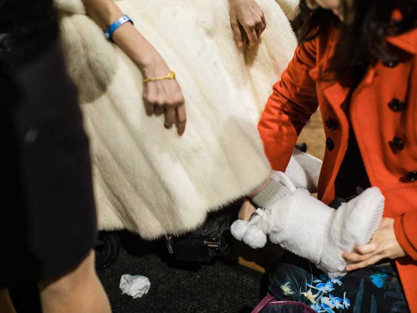 Woman placing white furry slipper on terminally ill bride's foot as she sits in wheelchair