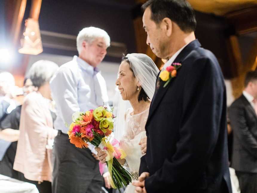 Terminally ill bride is walking down the aisle with her father as she smiles at someone in the crowd