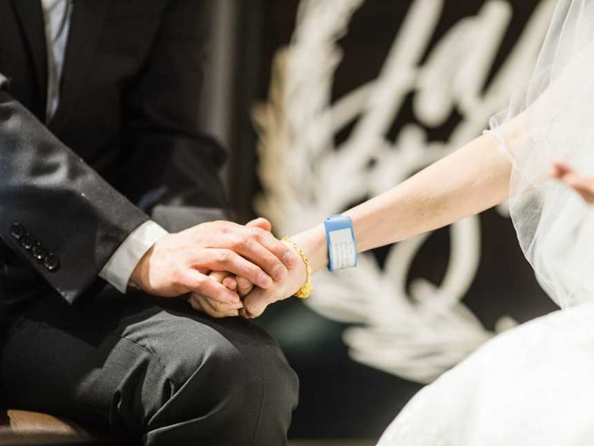 Close up of groom and terminally ill bride who has a hospital bracelet on holding hands