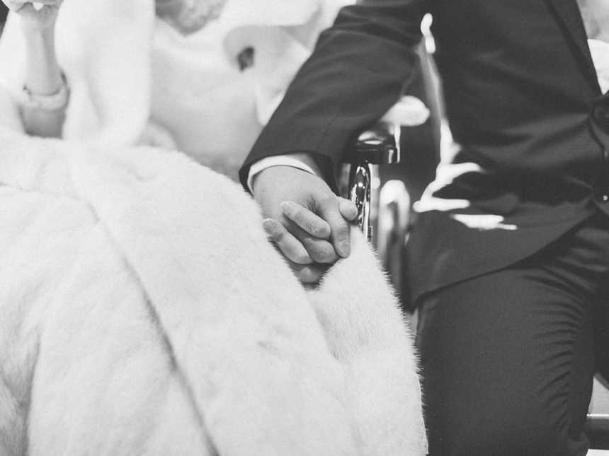 Close up of groom holding terminally ill bride's hand who is in wheelchair