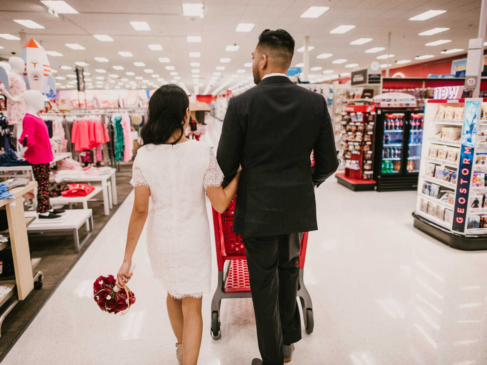 View from the back of bride and groom arm and arm while groom pushes shopping cart in Target